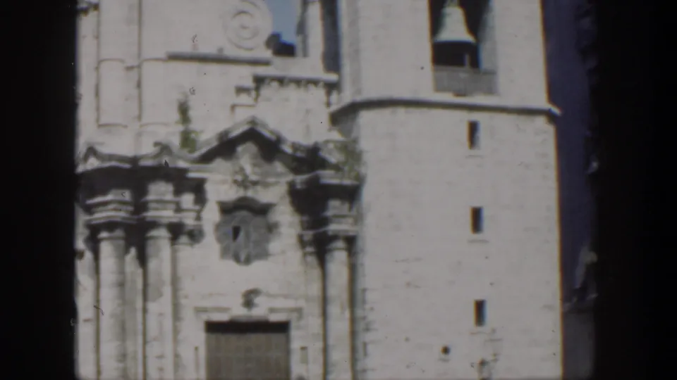 A Cuba 1951 frame shows the church's carved entrance and tall bell tower, with dark film borders and adjacent urban buildings visible.