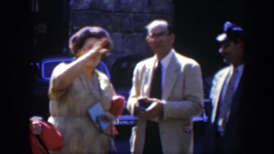 In a 1951 Cuba street scene, a woman in a patterned dress gestures near two suited men and parked cars.