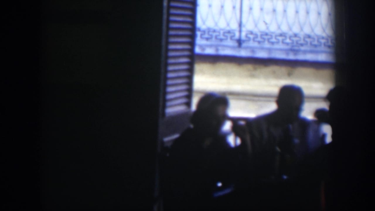 Adults sit in silhouette at a table before a bright window with shutters and metal grilles.