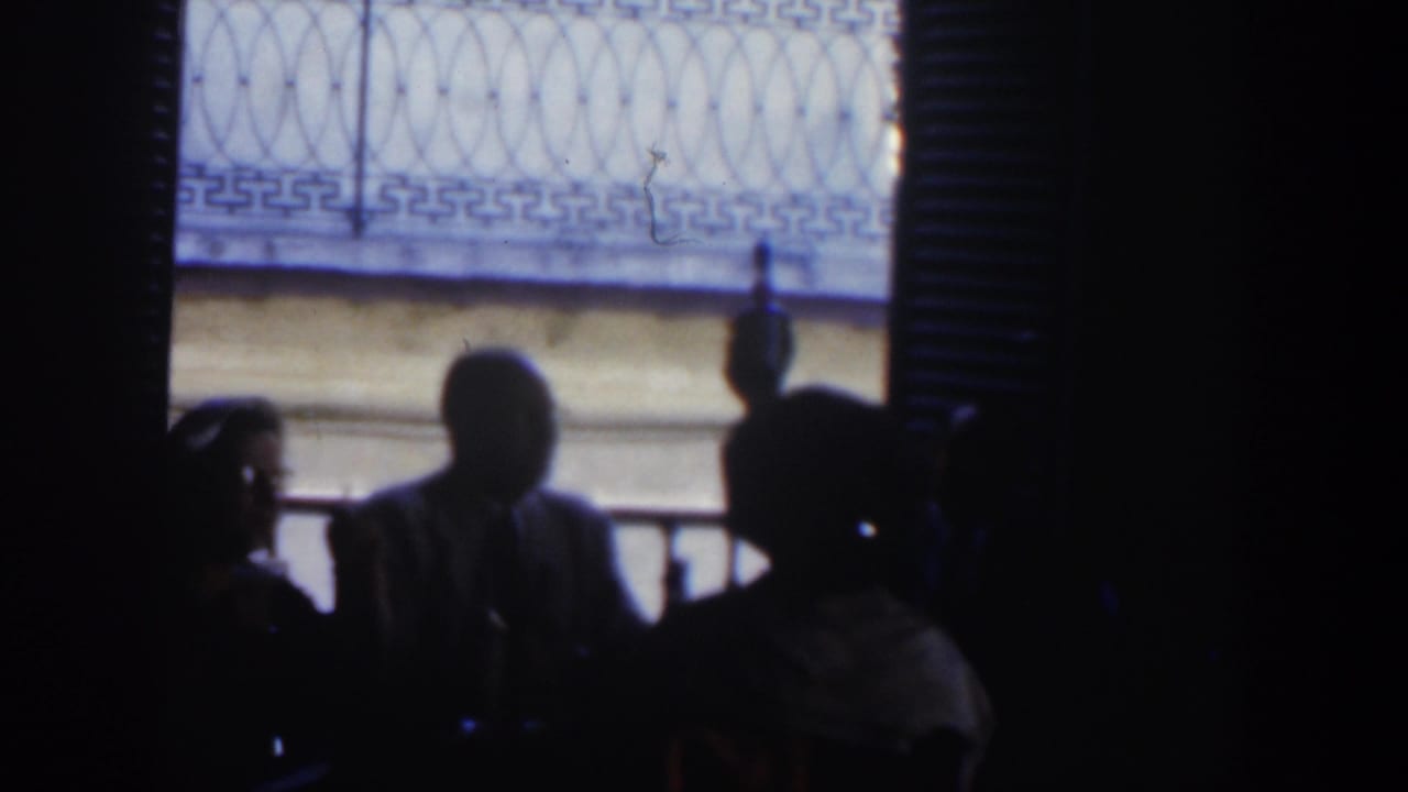 Several seated figures are silhouetted against a bright window inside a dim room.