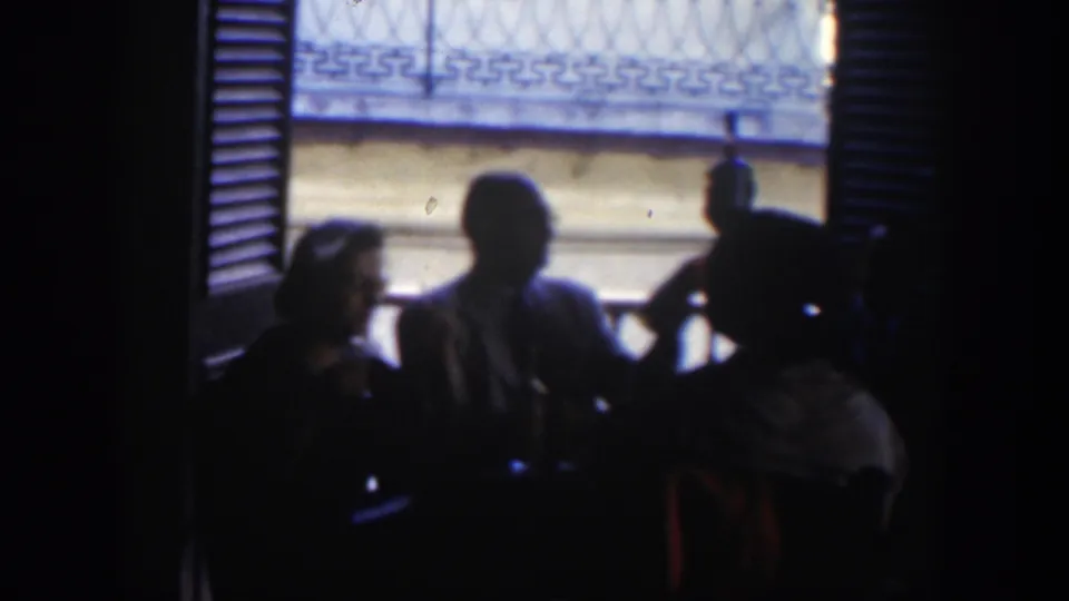 In a Cuba home-movie frame from 1951, a woman and man sit near a table while another figure is partly visible in the dim interior.