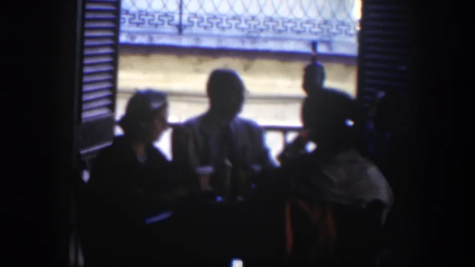The final frame shows adults gathered around a table in a dark Cuban interior, backlit by a bright window and metal grilles.