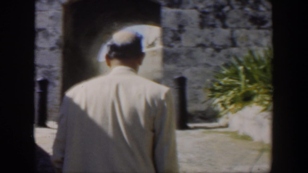 In 1951 Cuba home-movie footage, two adults in light clothing walk away through a sunlit stone courtyard.