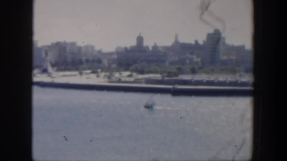 A soft 8mm view looks across Cuban harbor water toward a distant skyline, with a small boat visible near the center of the frame.