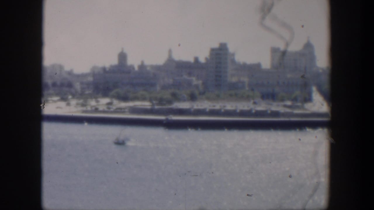 1951 Cuba 8mm view of a hazy coastal skyline across water, with domed buildings, a small boat, and dark framing edges.