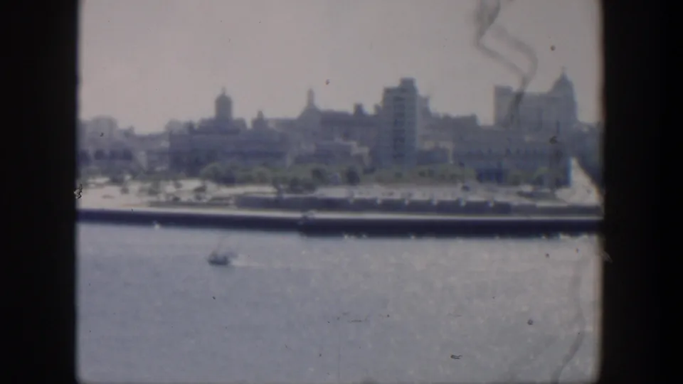 1951 Cuba 8mm view of a hazy coastal skyline across water, with domed buildings, a small boat, and dark framing edges.