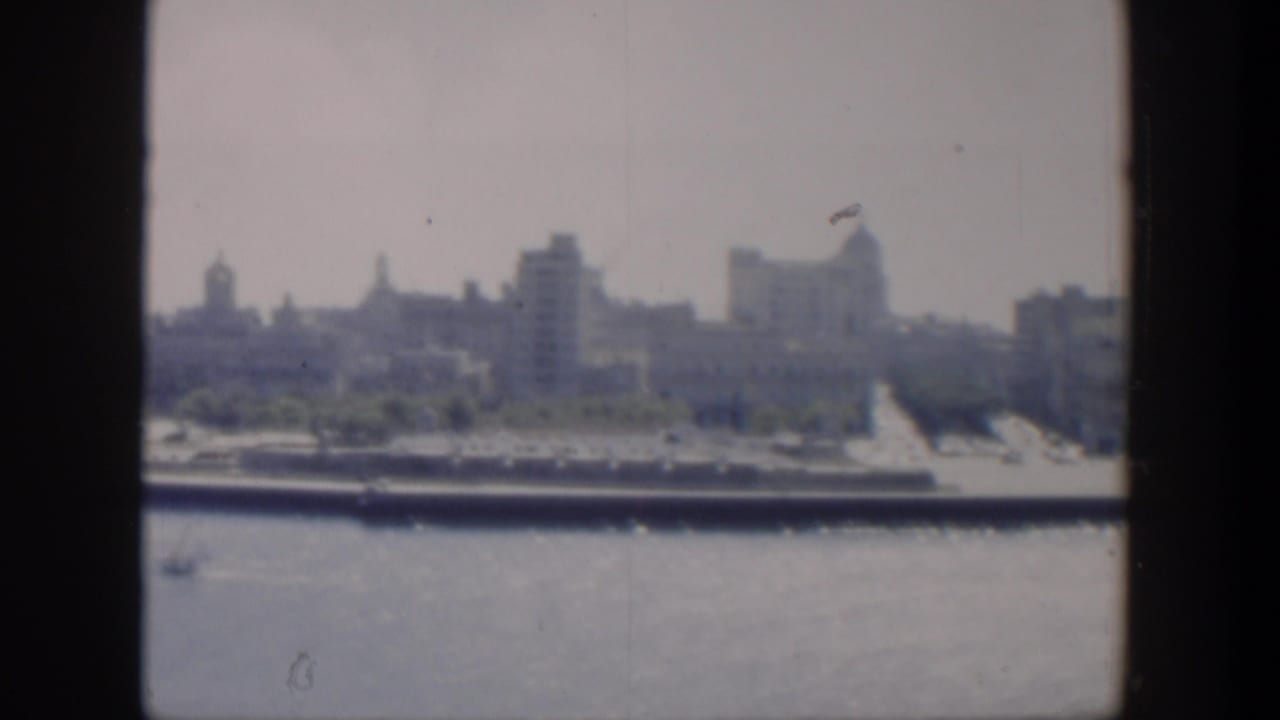 Coastal skyline seen across water with shoreline structures and dark vertical borders.
