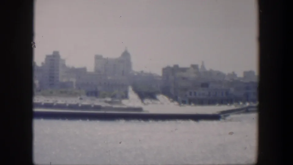 1951 Cuba 8mm view of waterfront buildings and domed rooflines across sunlit water, softened by haze and film grain.
