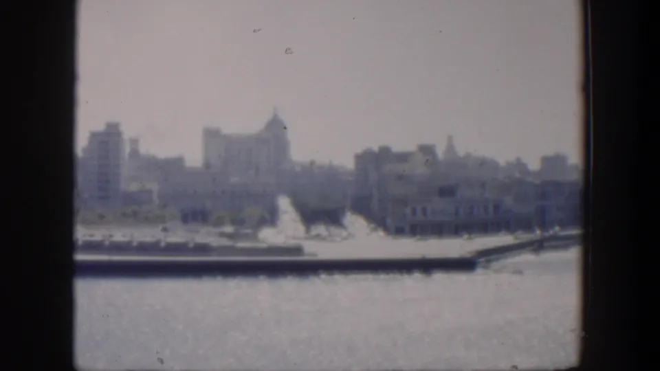 1951 Cuba 8mm frame showing a hazy distant waterfront cityscape across open water, with buildings and trees along the shore.