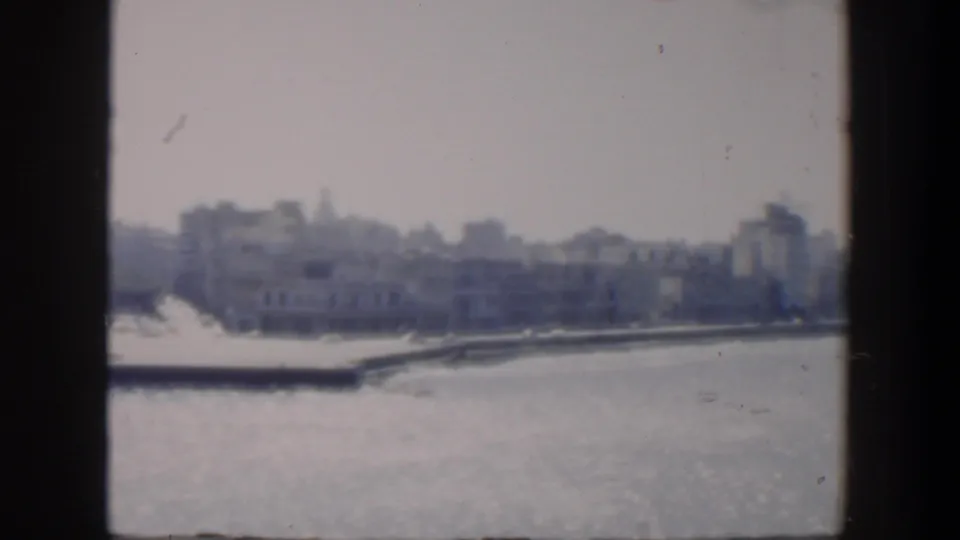 Distant Cuban waterfront in a 1951 home-movie frame, with low-rise buildings, trees, and bright water in the foreground.