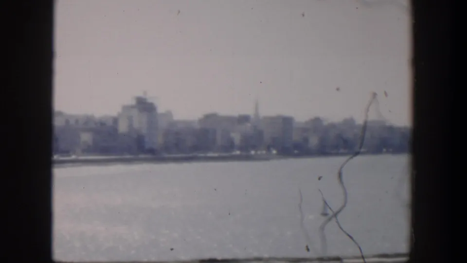 1951 Cuba frame with a hazy city shoreline, blue water, a distant church steeple, and 8mm dust and scratches.