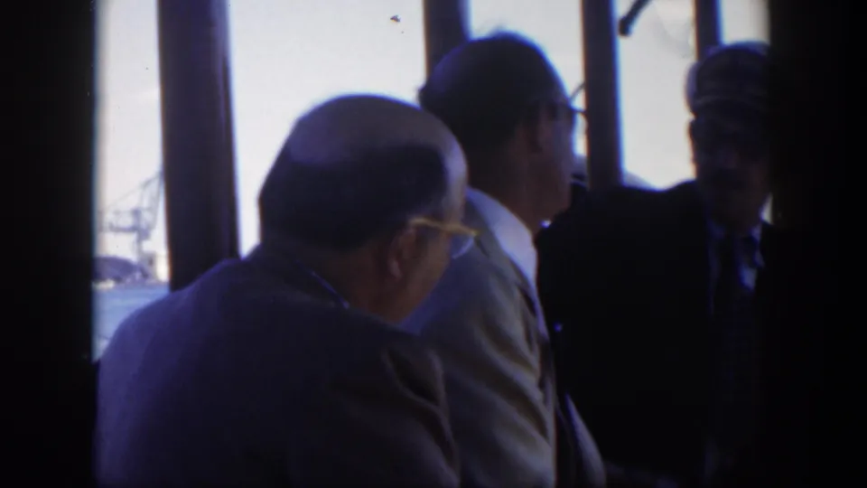 1951 Cuba boat interior with suited male passengers and a uniformed man near windows looking out toward the harbor.