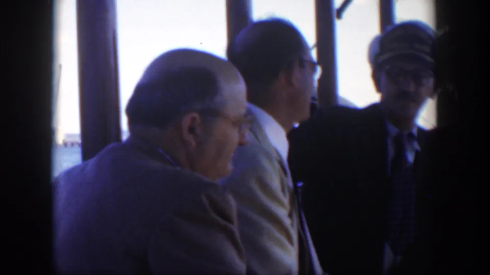 1951 Cuba ferry or boat interior with older suited passengers and a uniformed man framed against bright harbor windows.