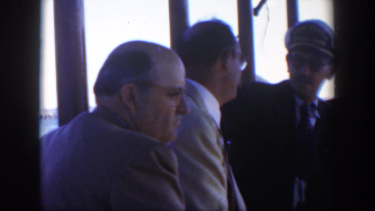 Three adult men in suits near bright ship windows, one older man seated in the foreground.