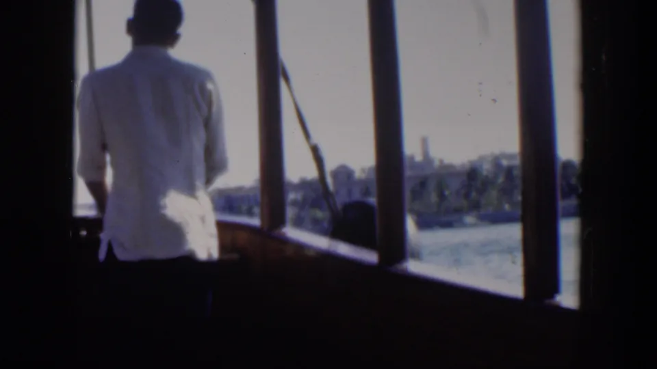 1951 Cuba 8mm frame showing a man from behind on a boat deck, with water and a distant coastal skyline beyond the windows.