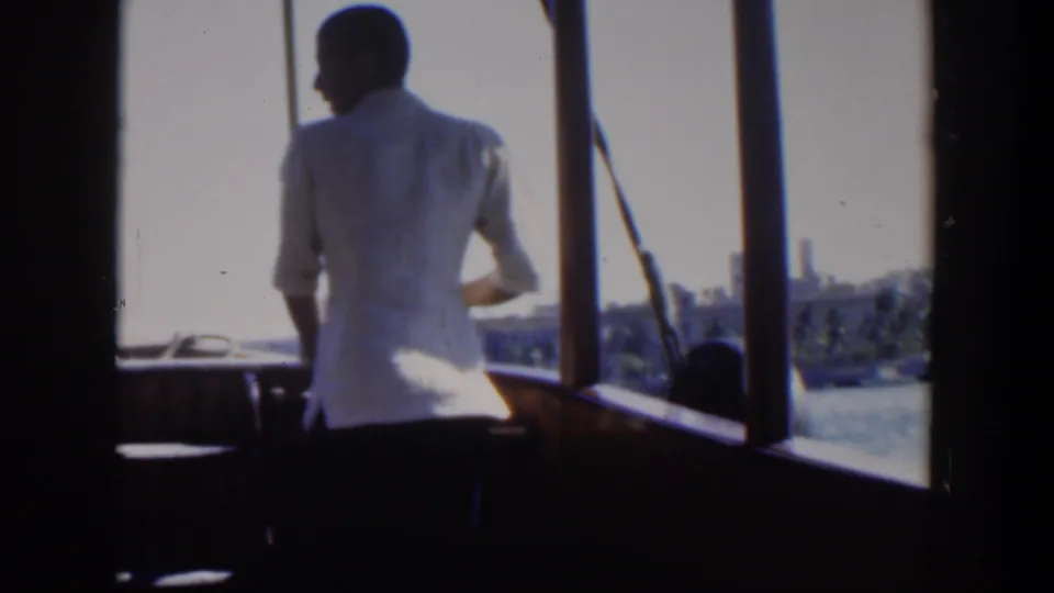 1951 Cuba 8mm frame with a man on a boat deck in partial profile, looking out toward water and a coastal city view.