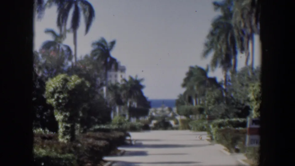 1951 Cuba 8mm frame showing a tropical garden walkway leading toward the ocean, framed by palms and shrubs.