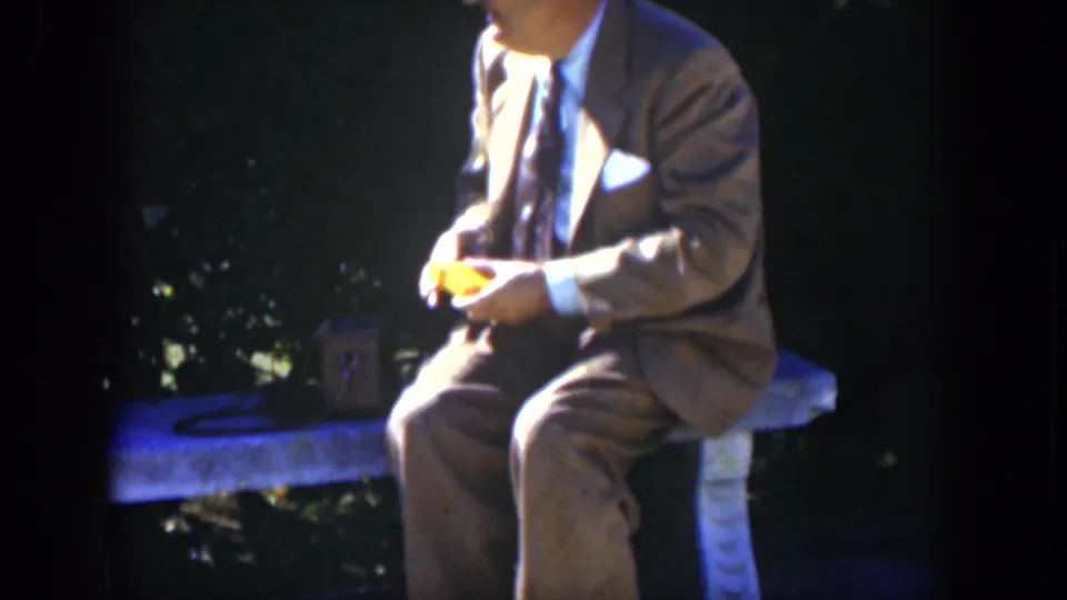 Closer 1951 Cuba home-movie frame of a suited man on a stone bench, his face partly cropped as he handles a yellow object.
