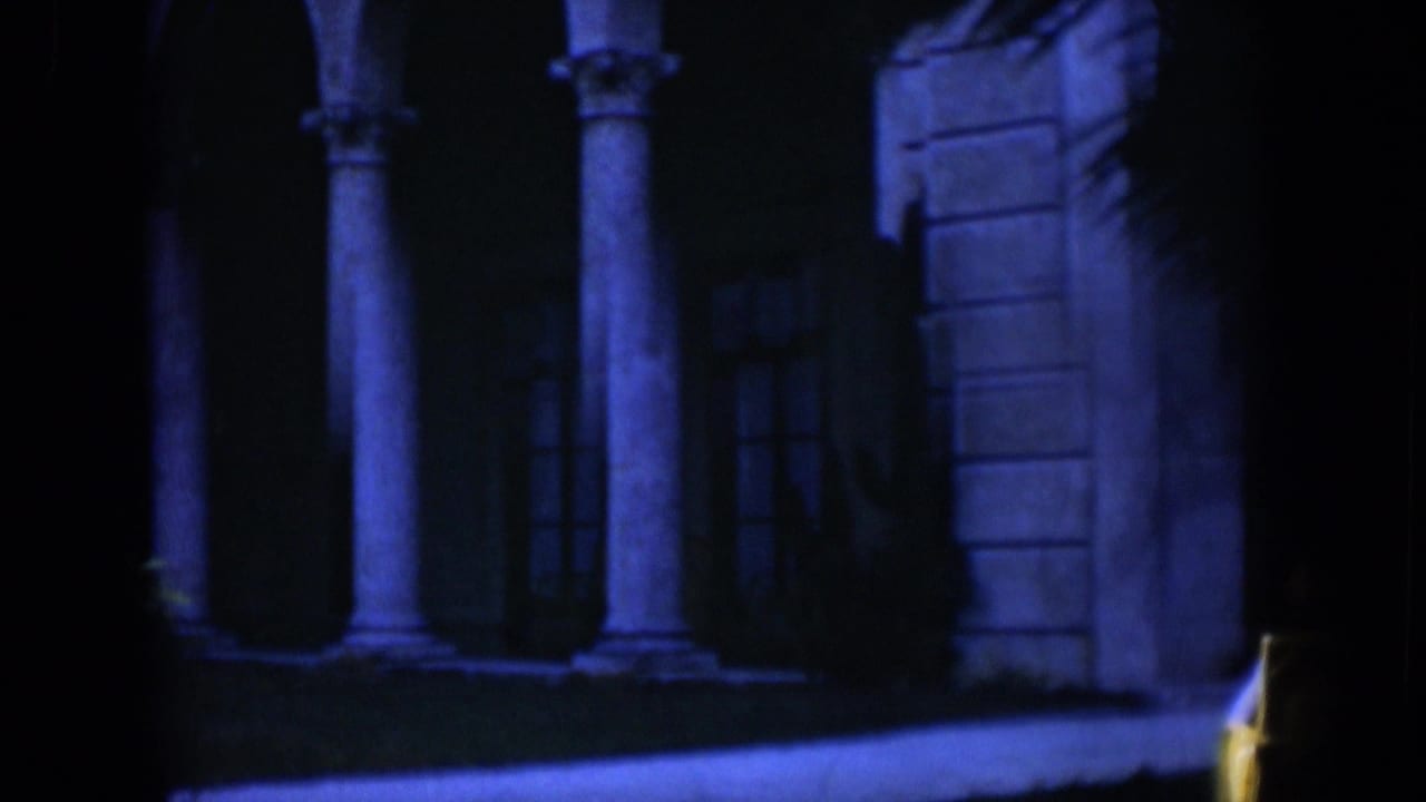 Dark blue-lit building facade with columns, arches, and a small figure near the center.