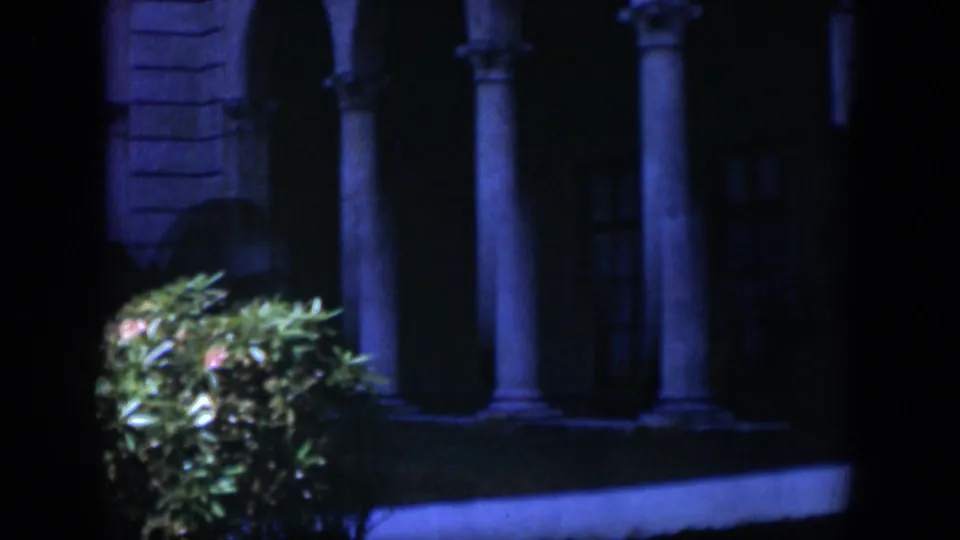 1951 Cuba frame with a formal columned building partly hidden by a lit shrub and heavy night shadow.