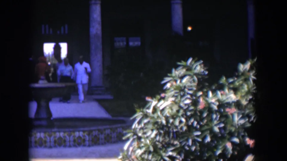 1951 Cuba courtyard frame with men walking past a tiled fountain, columns, plants, and a bright doorway beyond.