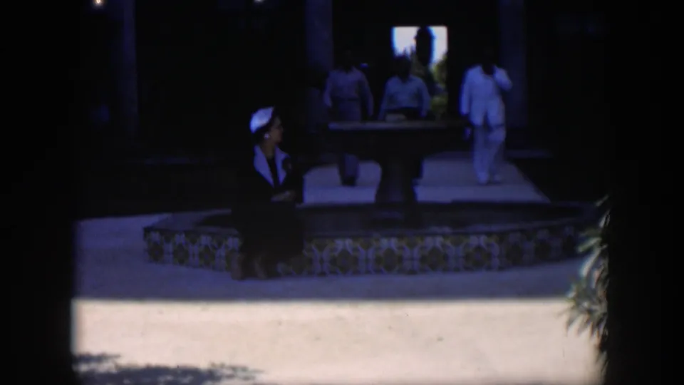 1951 Cuba courtyard frame showing a seated woman by a tiled fountain while several figures walk through the shadowed colonnade.