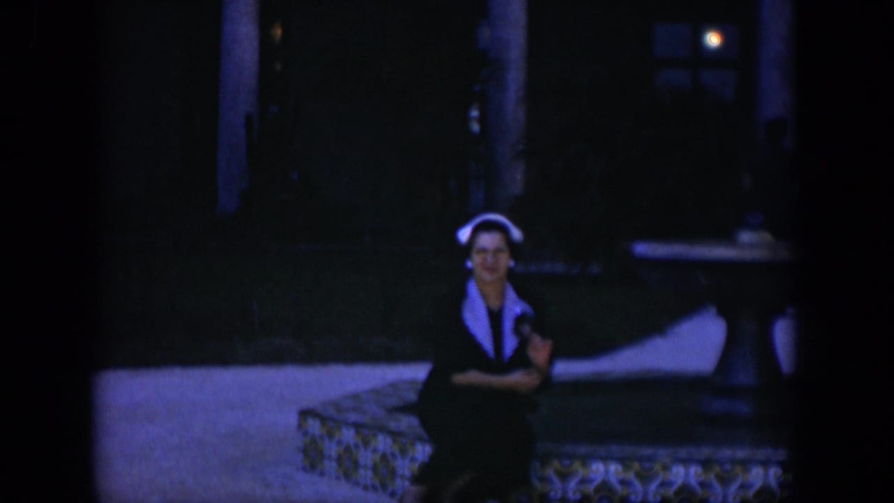 Woman in a white headscarf sits on a tiled bench in a dim courtyard.
