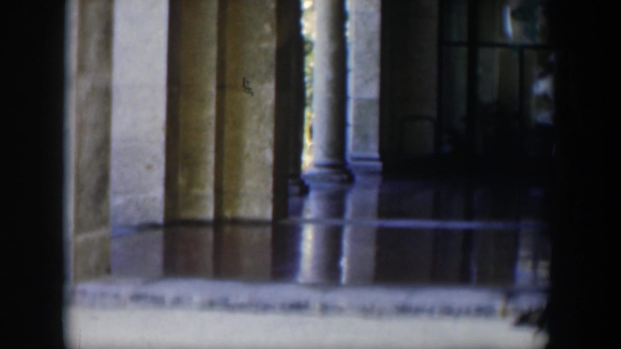 Stone columns and a reflective floor are seen in a dim building entrance.
