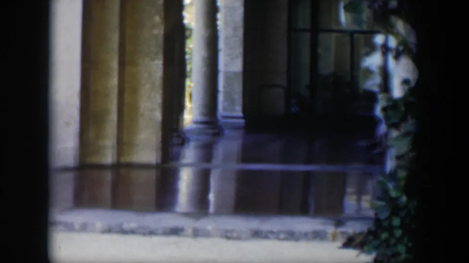 The 1951 Cuba home-movie frame shows a shadowed portico with columns, a dark window and leafy foreground growth.