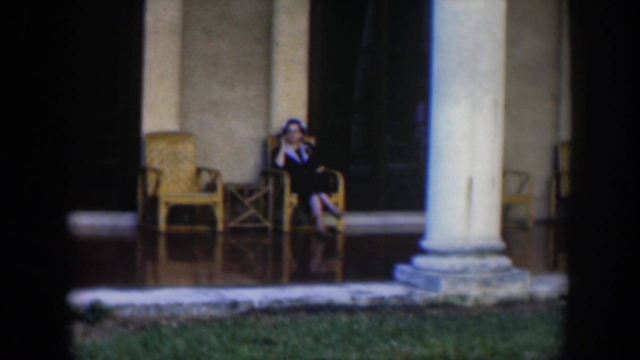 In 1951 Cuba footage, a woman sits on a tiled porch near wicker furniture and large columns.
