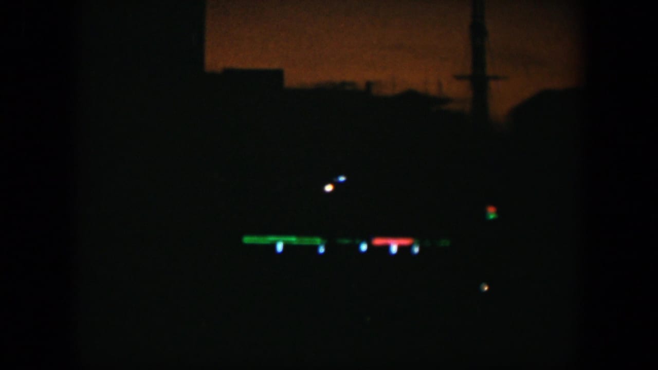 1951 Cuba 8mm frame showing a dark exterior with distant green, red, and blue lights below a faint orange sky.