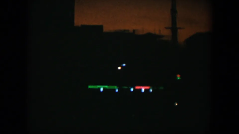 1951 Cuba 8mm frame showing a dark exterior with distant green, red, and blue lights below a faint orange sky.