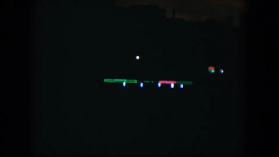 Grainy 8mm night frame from Cuba in 1951 with colored lights set against deep shadow and faint structural silhouettes.