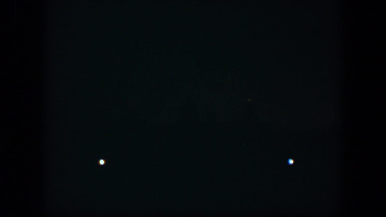 1951 Cuba 8mm frame showing a mostly black night scene with two isolated white lights and dim points near the bottom.