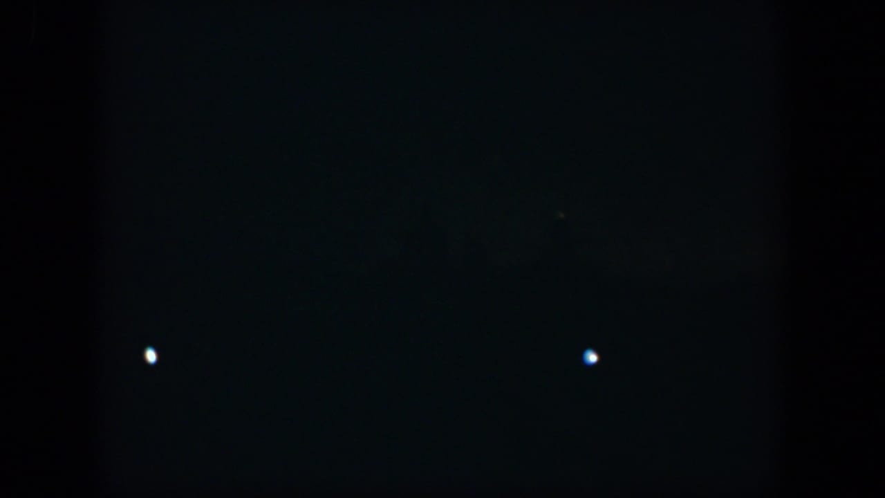 Dark frame with a bright white dot and faint lights near the lower edge.