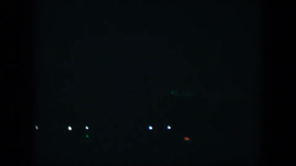 1951 Cuba 8mm frame with low scattered lights, a faint green glow, and a small red-orange point in the darkness.