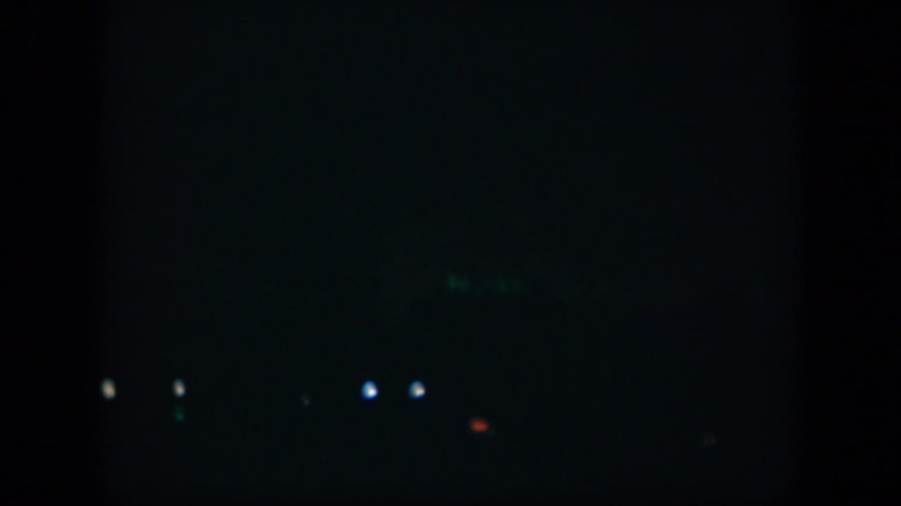 1951 Cuba 8mm frame showing a very dark exterior with isolated points of light and a faint green PARK sign in the distance.