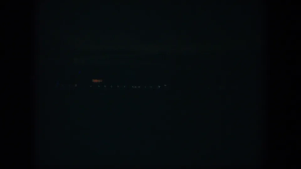 Final low-light 8mm frame from the Cuba clip, showing scattered distant lights against a nearly black exterior view.