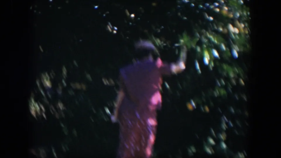 A motion-blurred 8mm frame shows the woman moving beside the citrus foliage during the 1951 Cuba home movie.
