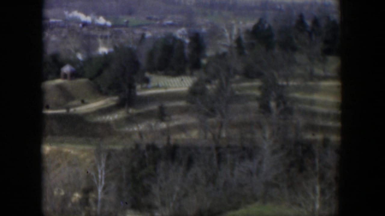 Soft aerial view over hills, trees, open fields, and a small distant structure.