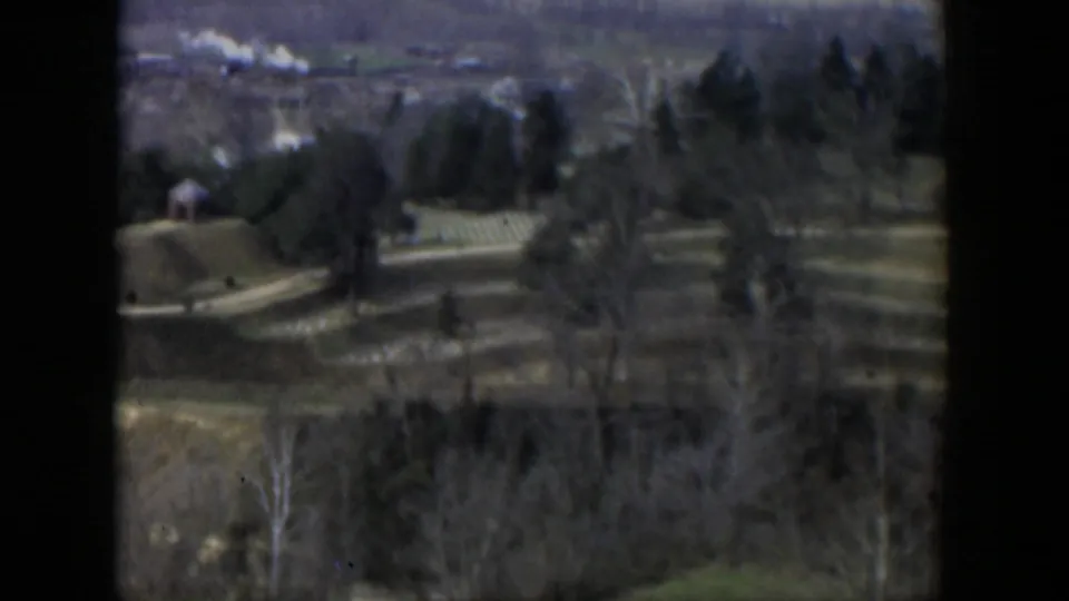1951 Cuba 8mm aerial view showing rolling rural terrain, scattered trees, fields, and a small structure in the distance.