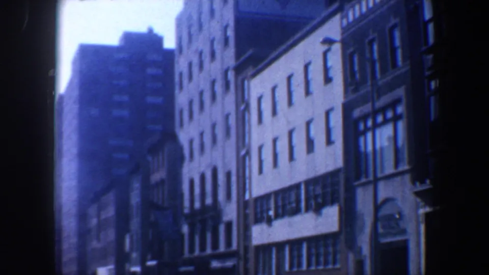 1962 Philadelphia frame showing a mid-century block with tall facades, storefront-like windows, parked cars, and film-edge shadow.