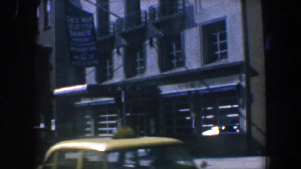 1962 Philadelphia street scene with storefronts, fire escapes, a dance-related sign, and a yellow taxi moving across the foreground.