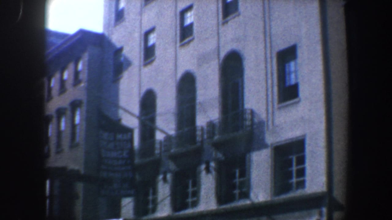 Closer angled view of the building facade with arched windows, fire escapes, storefronts, and a hanging sign.
