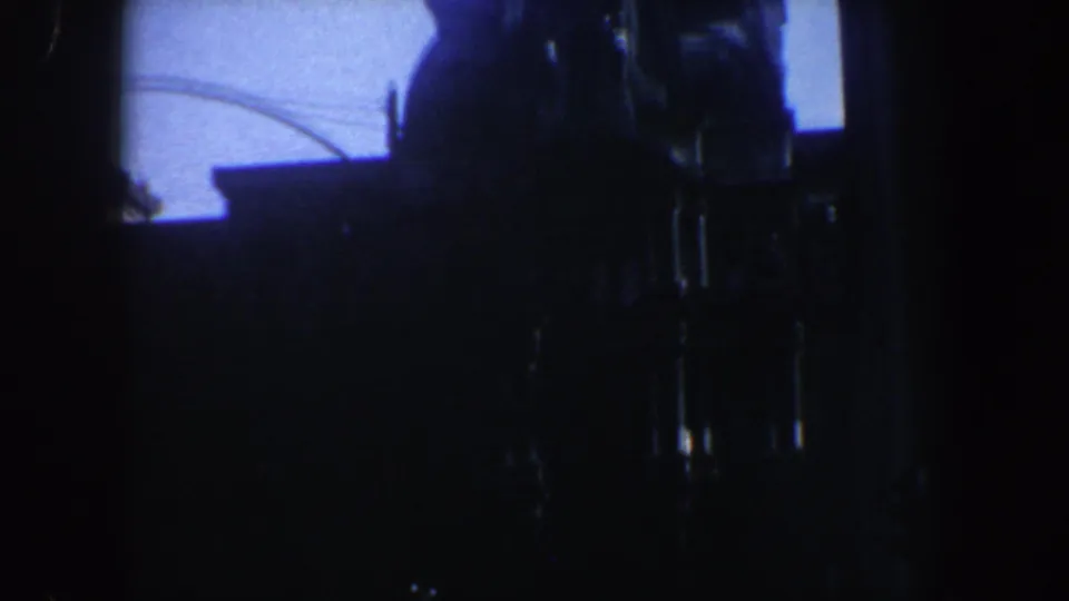 1962 Philadelphia home-movie frame with a dark monument-like silhouette set against a blue dusk sky and heavy 8mm grain.