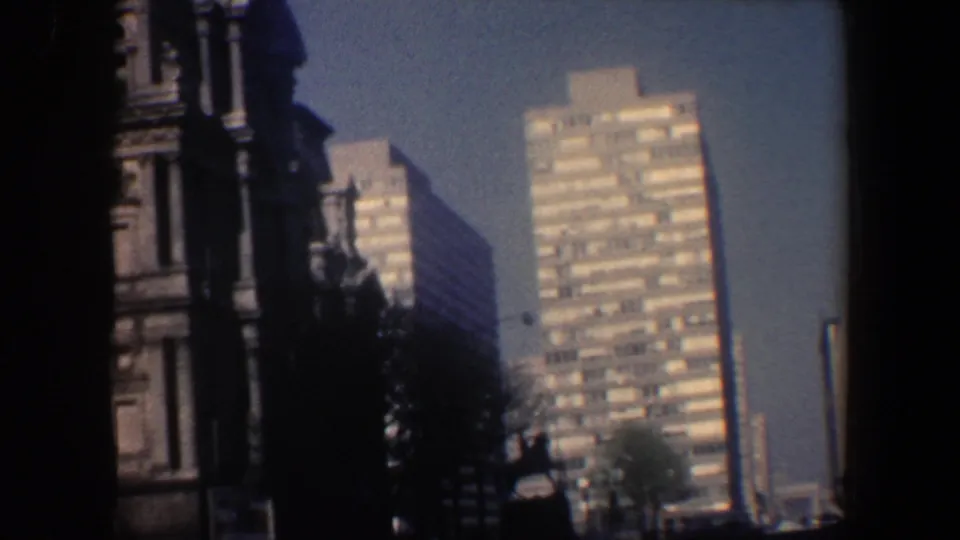 1962 Philadelphia street-level frame with a shadowed ornate stone facade and sunlit modern high-rise towers behind it.