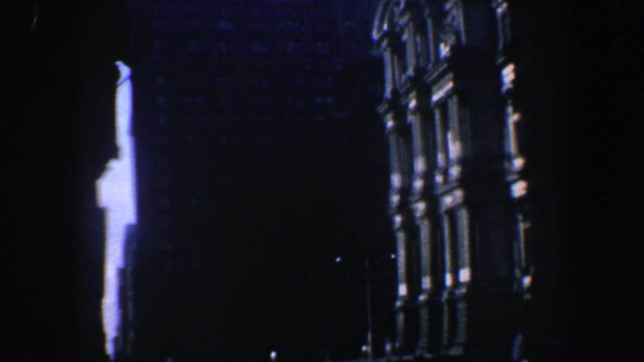 Shadowed night view of a tall ornate building exterior with bright vertical light.