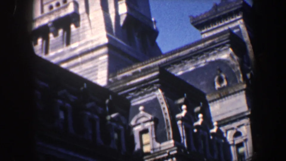 1962 Philadelphia home-movie frame showing the historic building in daylight, with a tower-like section, dormers, carved masonry, and blue sky.