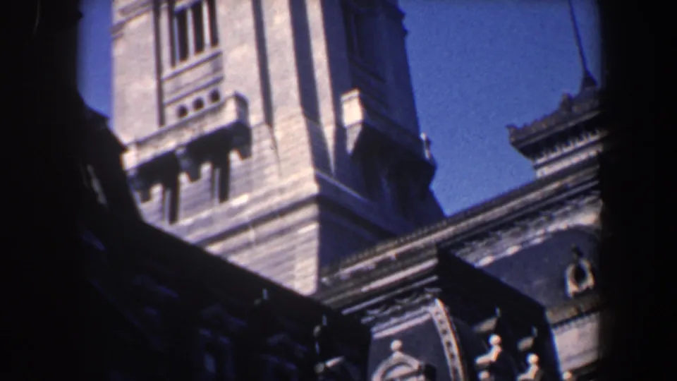 1962 Philadelphia 8mm frame showing pale stone tower sections, arched architectural details, and dark foreground edges against a clear blue sky.
