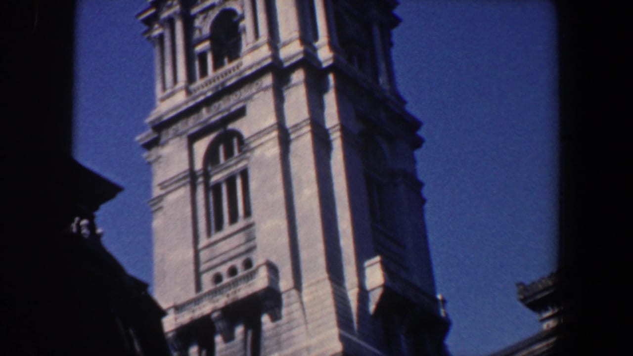 Tall stone tower with arched windows and decorative ledges against a blue sky.